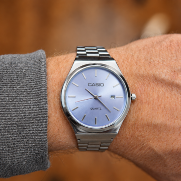 Reloj analógico plateado con esfera azul violácea y fechador, colocado en una muñeca.