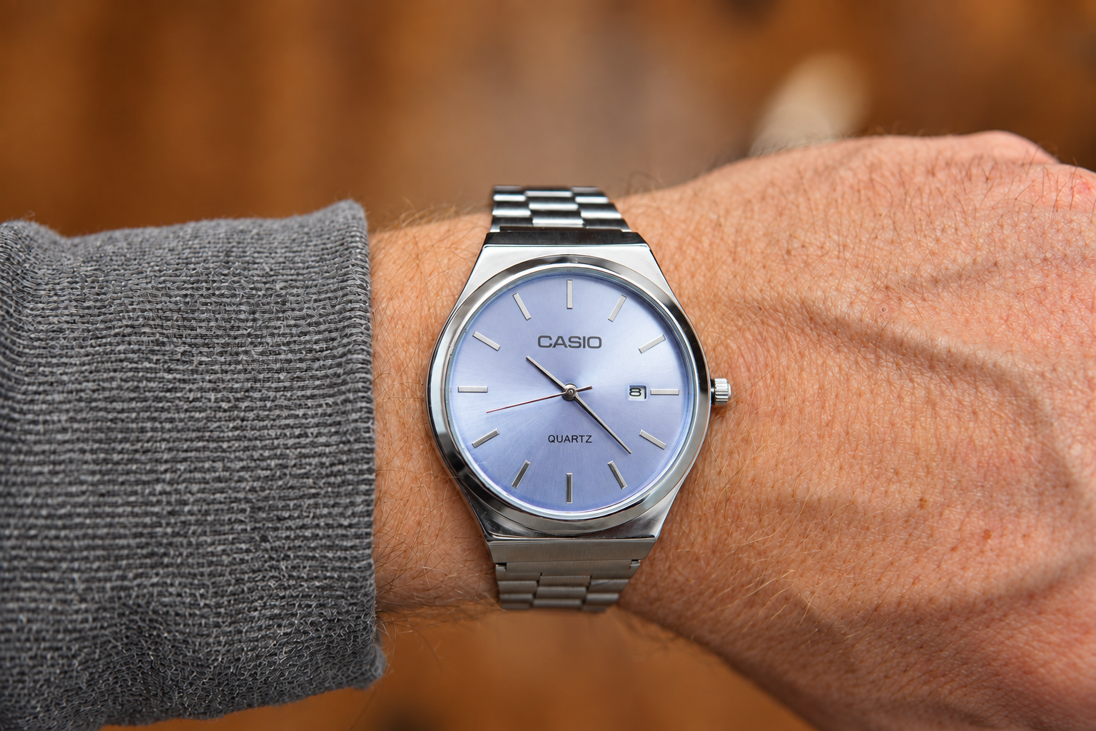 Reloj analógico plateado con esfera azul violácea y fechador, colocado en una muñeca.
