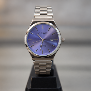 Reloj analógico plateado con malla de eslabones, esfera azul violácea y fechador lateral.