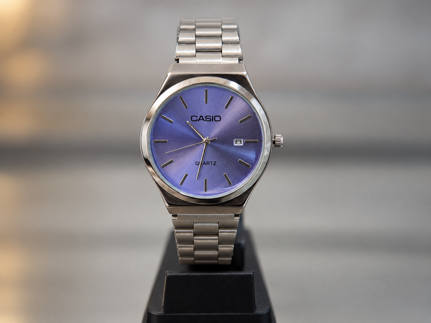 Reloj analógico plateado con malla de eslabones, esfera azul violácea y fechador lateral.